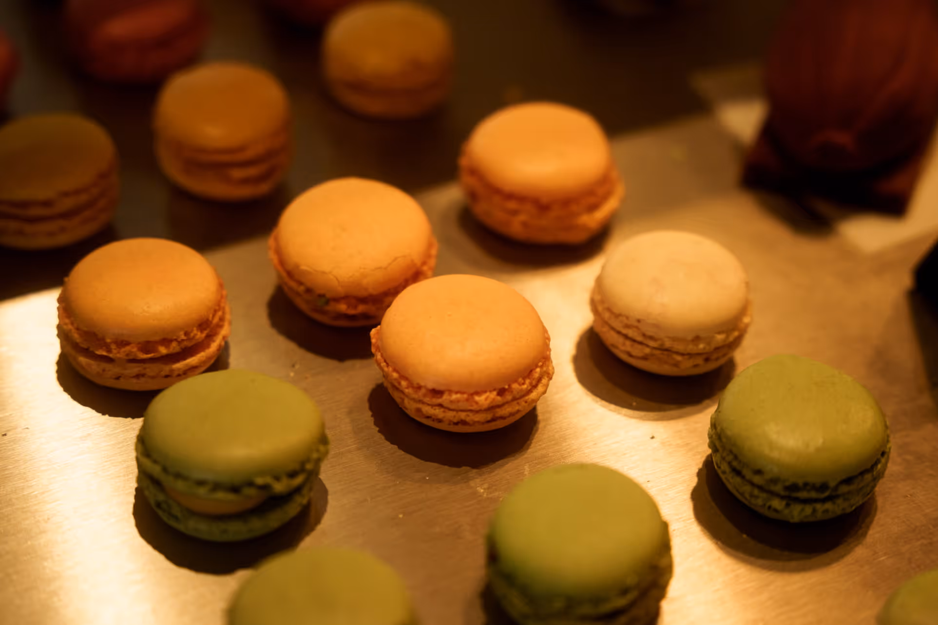 Verschiedene bunte Macarons auf einer Metallplatte, beleuchtet mit warmem Licht.