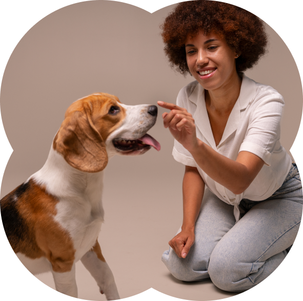 Smiling woman kneeling and pointing her finger at a beagle dog with its tongue out.