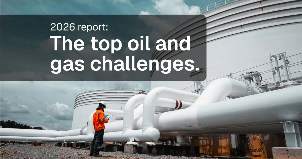 Oil and gas worker in an orange safety suit and hard hat inspecting white storage tanks and pipework at a refinery under a cloudy sky.
