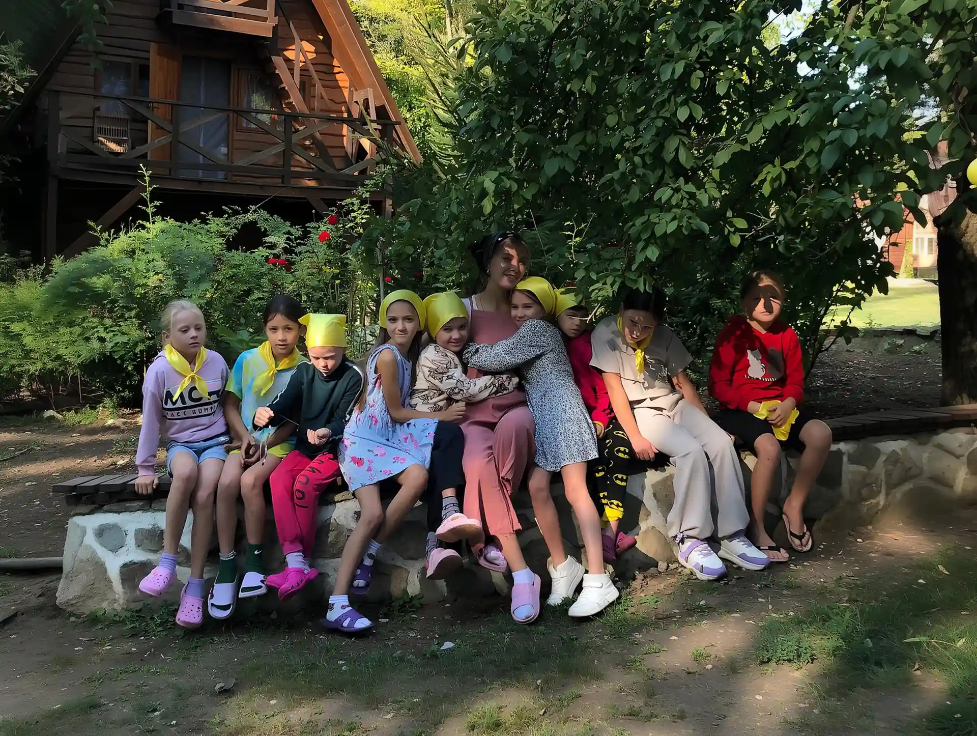 Дівчата з вихователькою сидять на кам'яному парапеті на території літнього табору «Шанс»