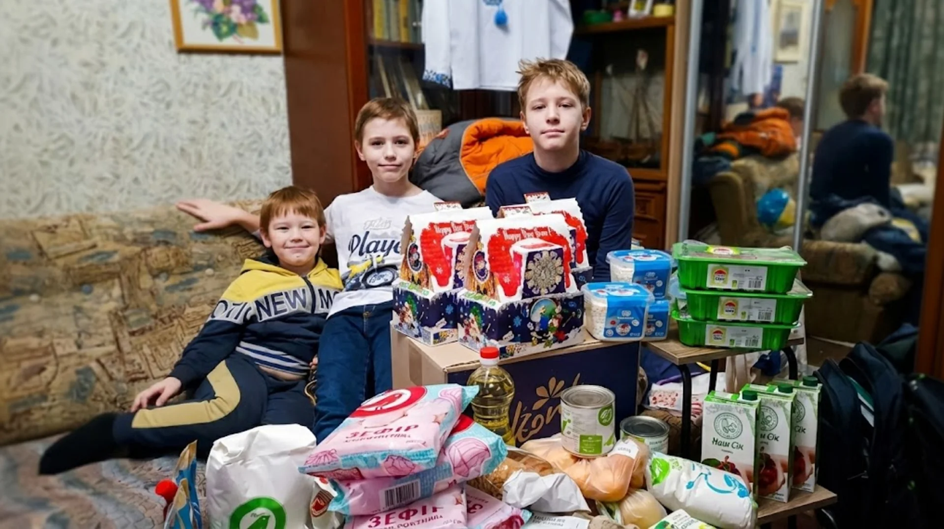 Діти сидять поруч із новорічними подарунками та продуктовими наборами.