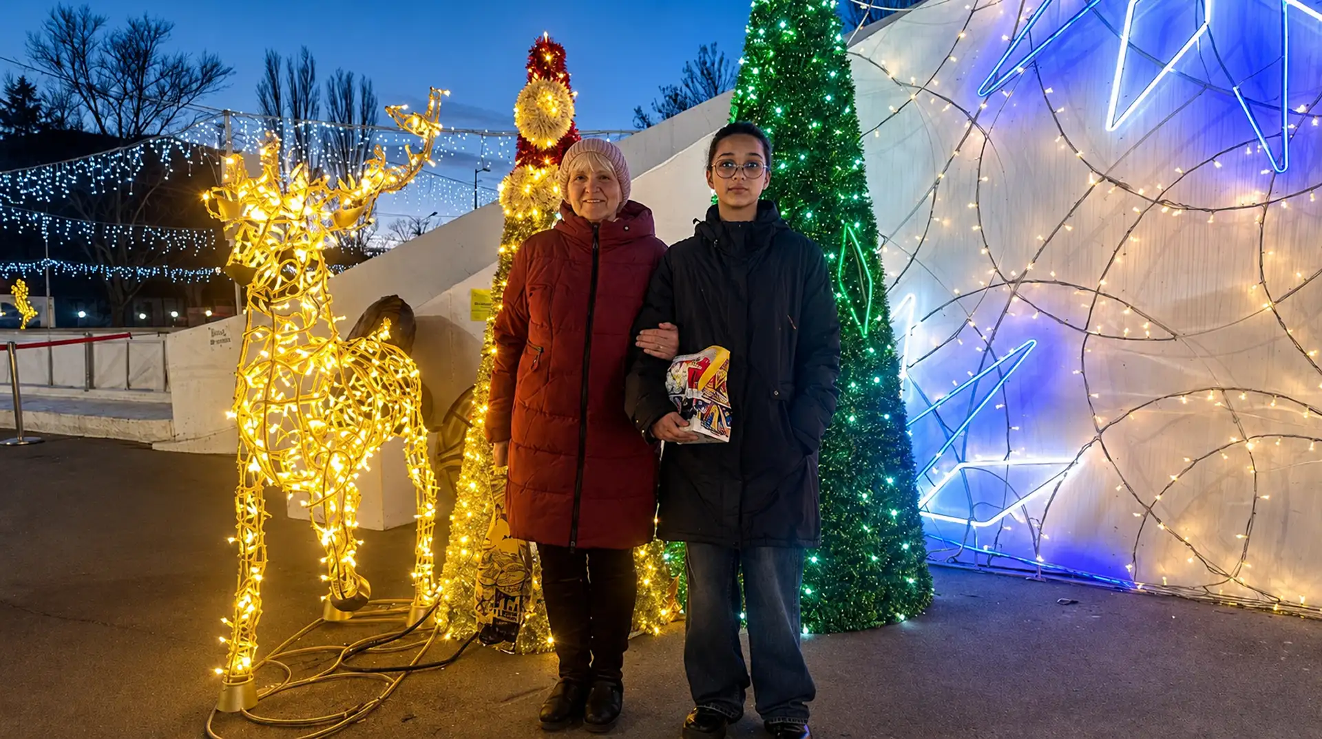  Дівчина стоїть біля святкових вогників із новорічним подарунком у руках.