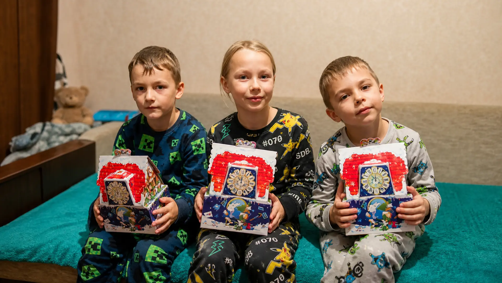 Троє дітей у піжамах тримають новорічні подарунки.