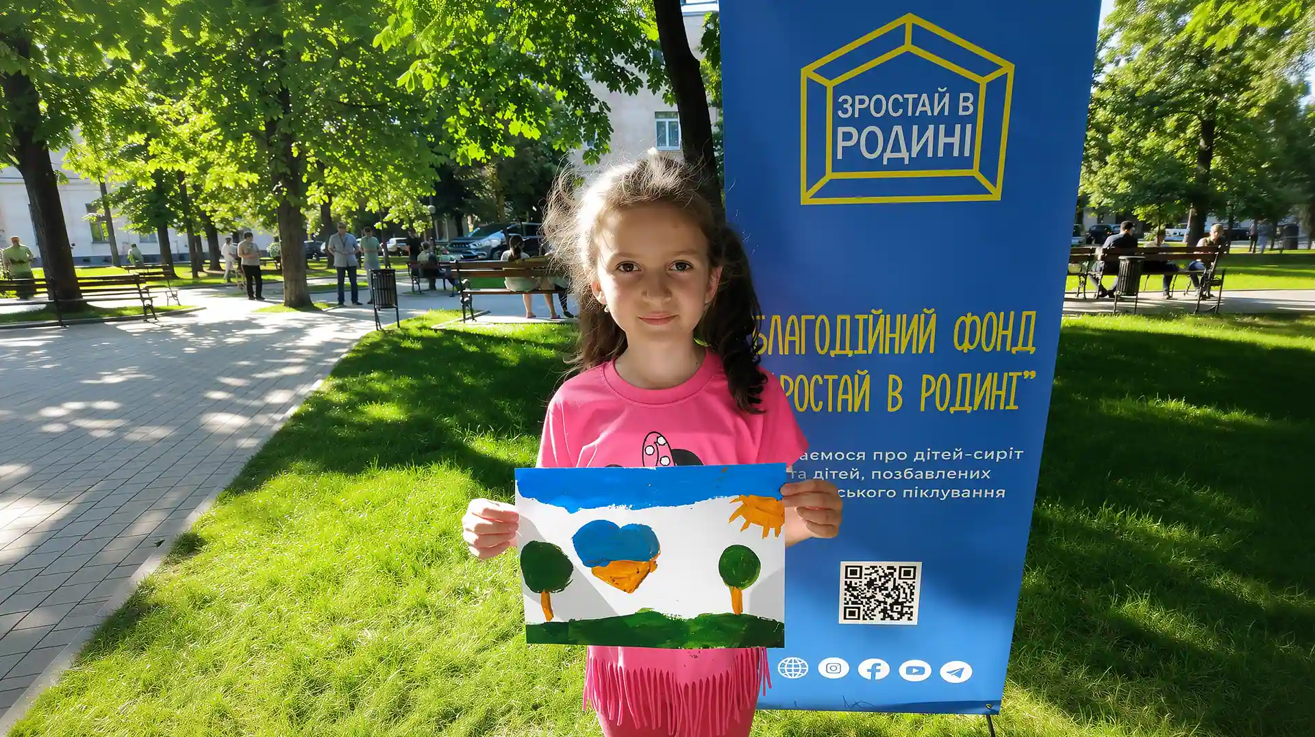 Дівчинка тримає малюнок біля банера фонду «Зростай в родині» у Кременчуці.