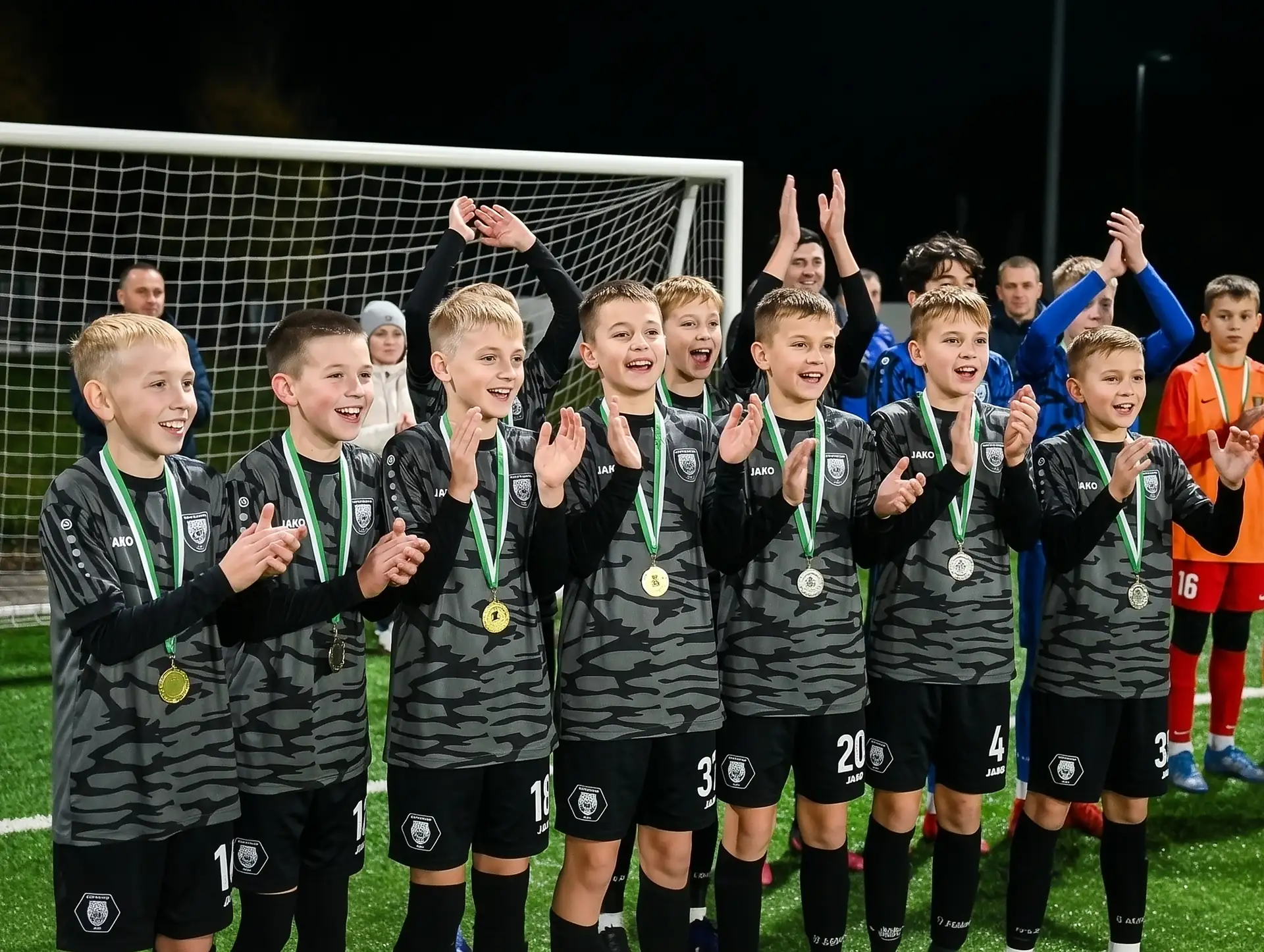 Юні футболісти в чорній формі з медалями аплодують під час церемонії нагородження.
