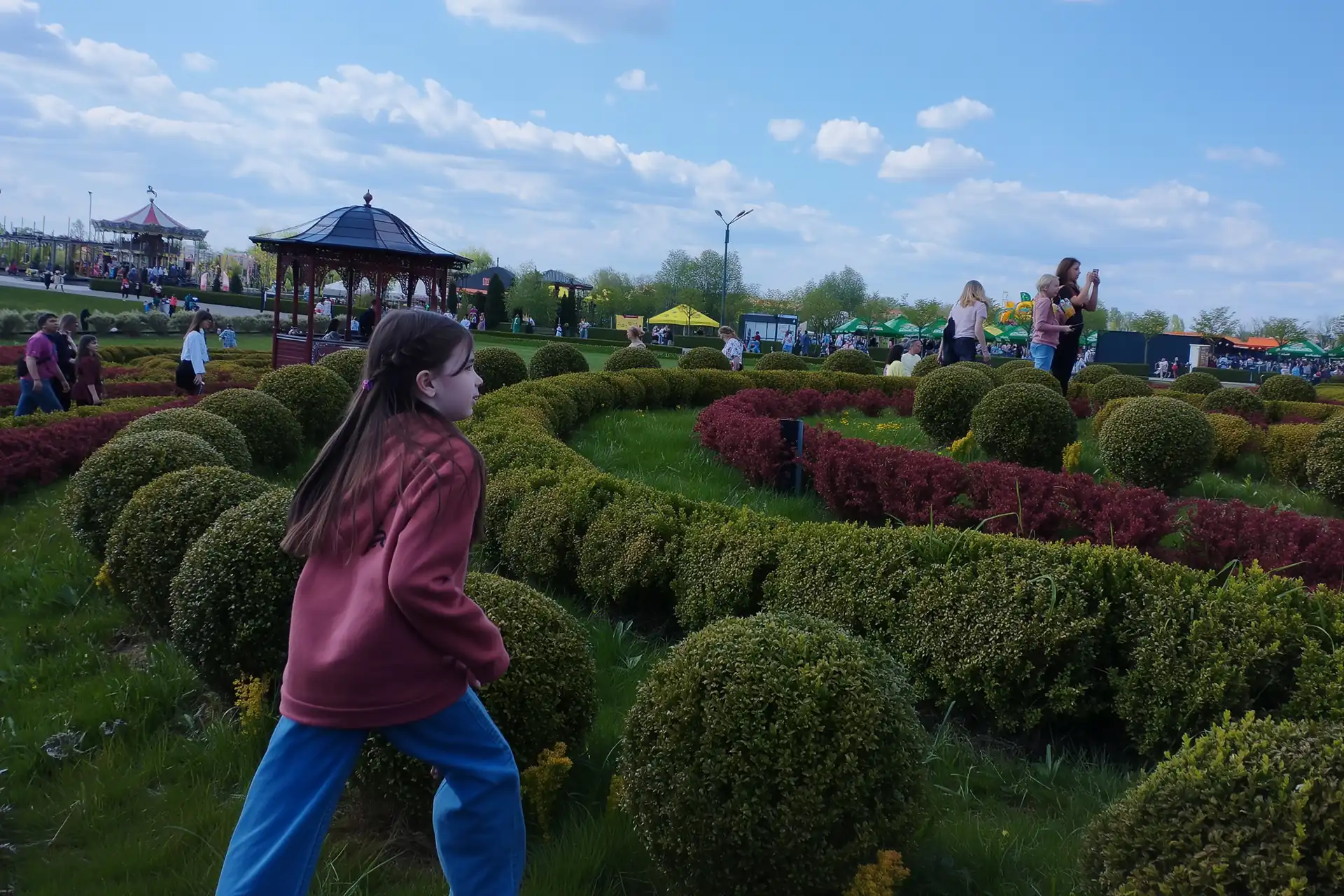 Дівчинка гуляє серед декоративних кущів і квітників у «Добропарку».