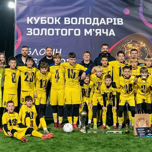 Дитяча футбольна команда позує біля банера Кубка володарів золотого мʼяча.