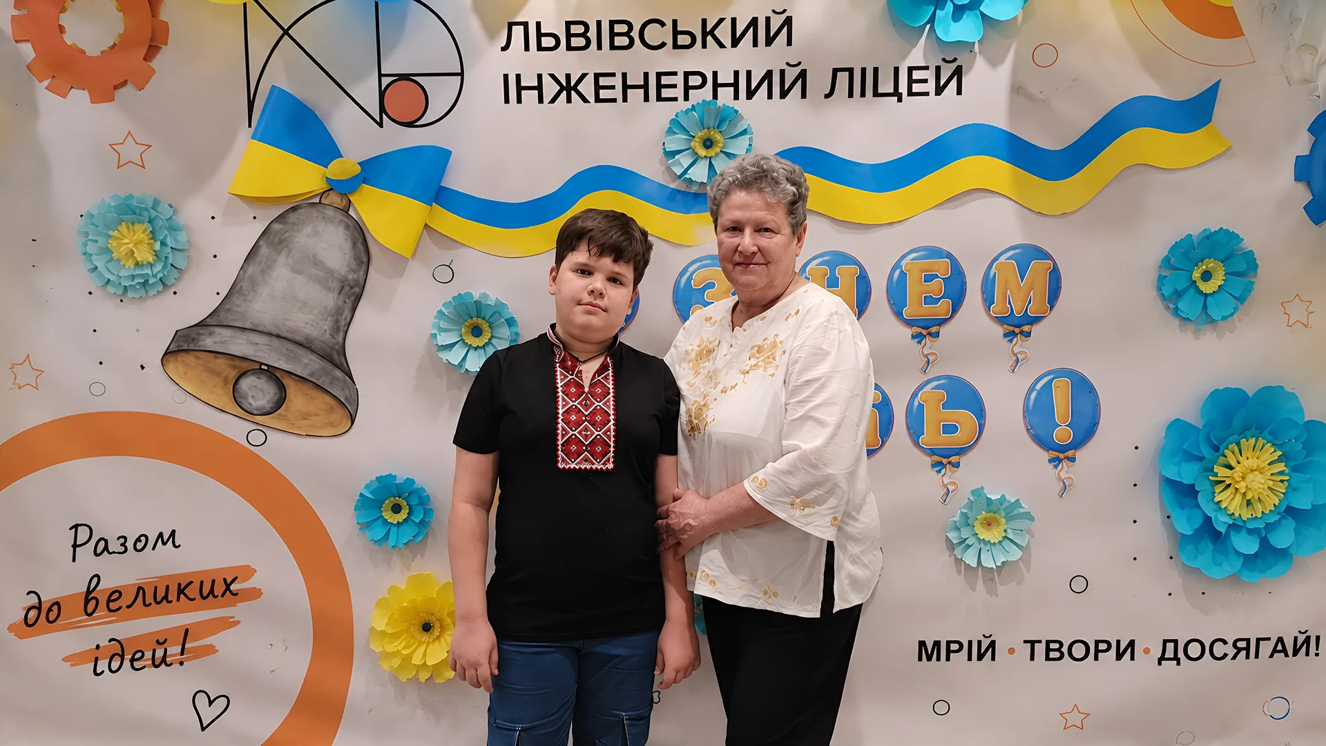 Хлопчик і жінка позують на святковому тлі Львівського інженерного ліцею.