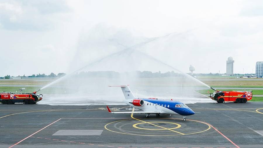 European Air Ambulance aircraft receiving a ceremonial water salute from airport fire trucks.