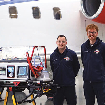 European Air Ambulance medical team standing beside a neonatal transport incubator in front of an air ambulance aircraft.