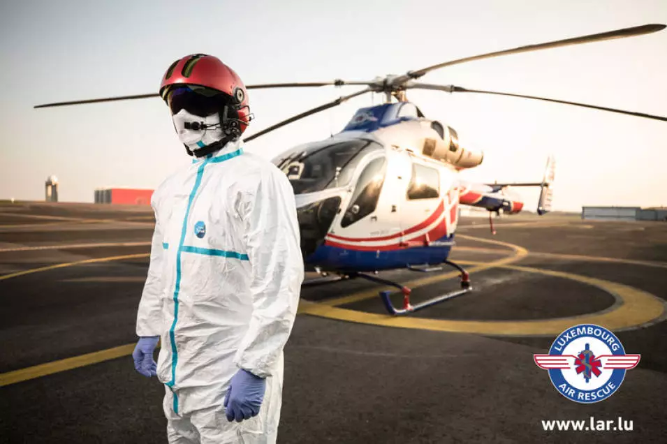 Luxembourg Air Rescue helicopter with crew member wearing protective gear during an emergency medical aviation operation.
