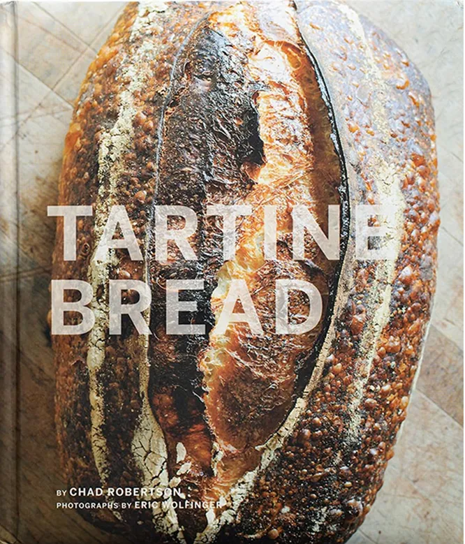 Close-up of a crusty, artisanal loaf of tartine bread on a wooden surface.