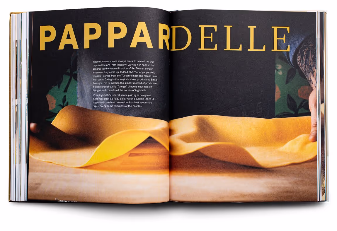Open book showing a page with large yellow text 'Pappardelle' and a close-up image of hands stretching fresh pasta dough.