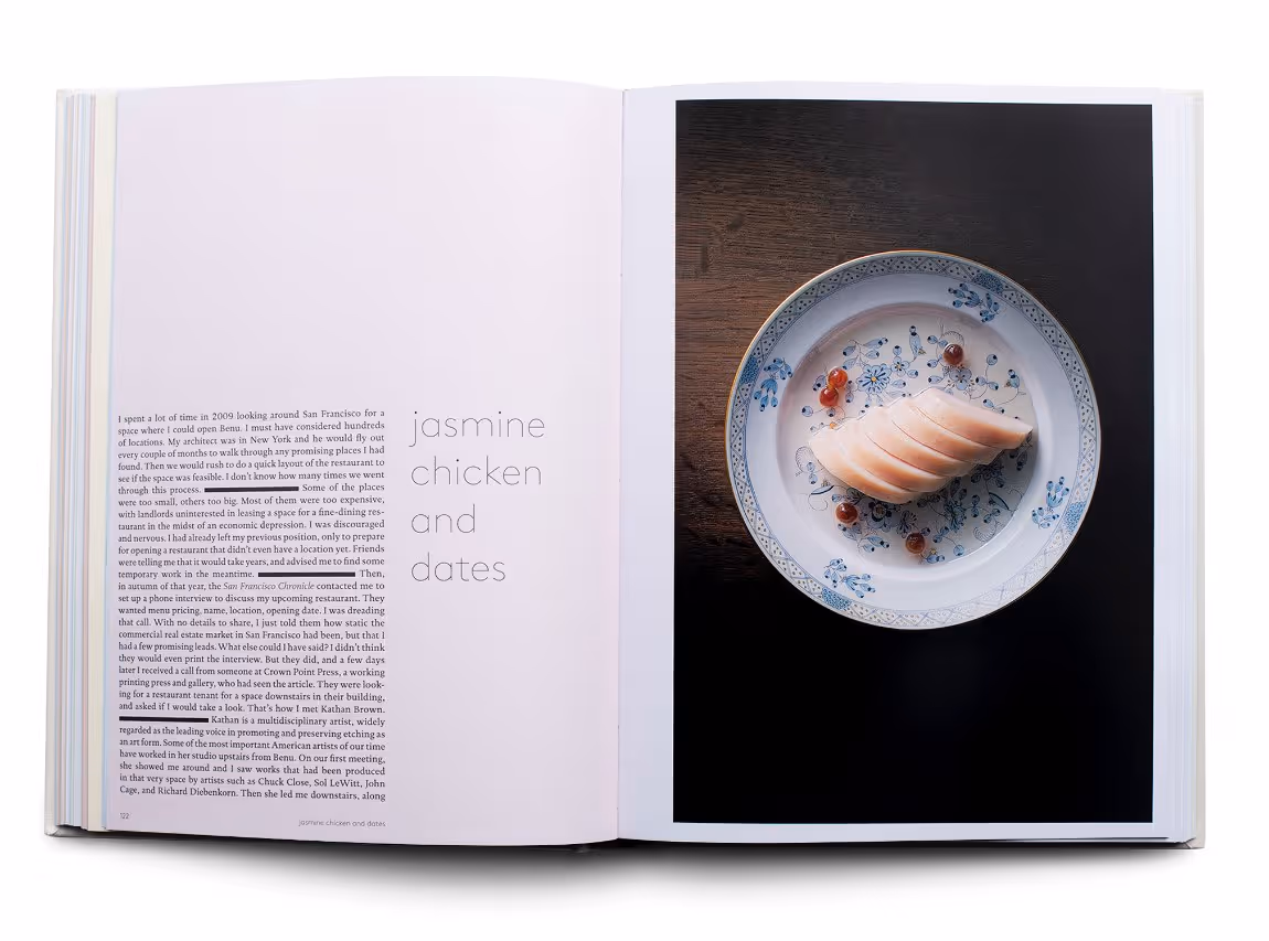 Open book showing text titled 'jasmine chicken and dates' on the left page and a dish with sliced chicken and berries on a blue-patterned plate on the right page.