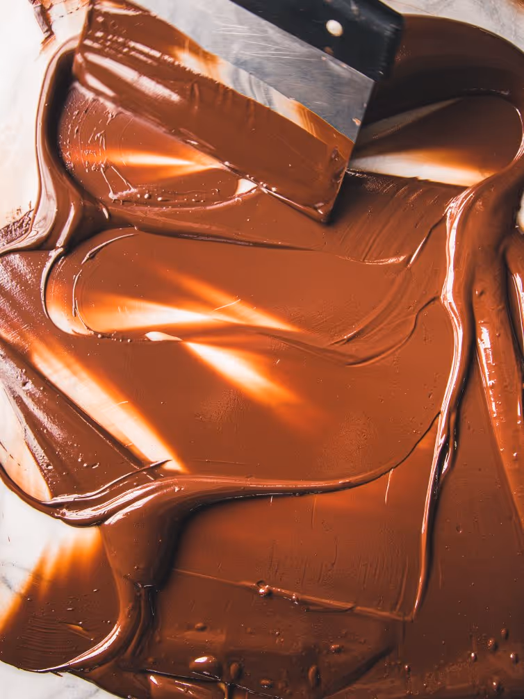 A metal spatula spreading smooth melted chocolate on a flat surface.