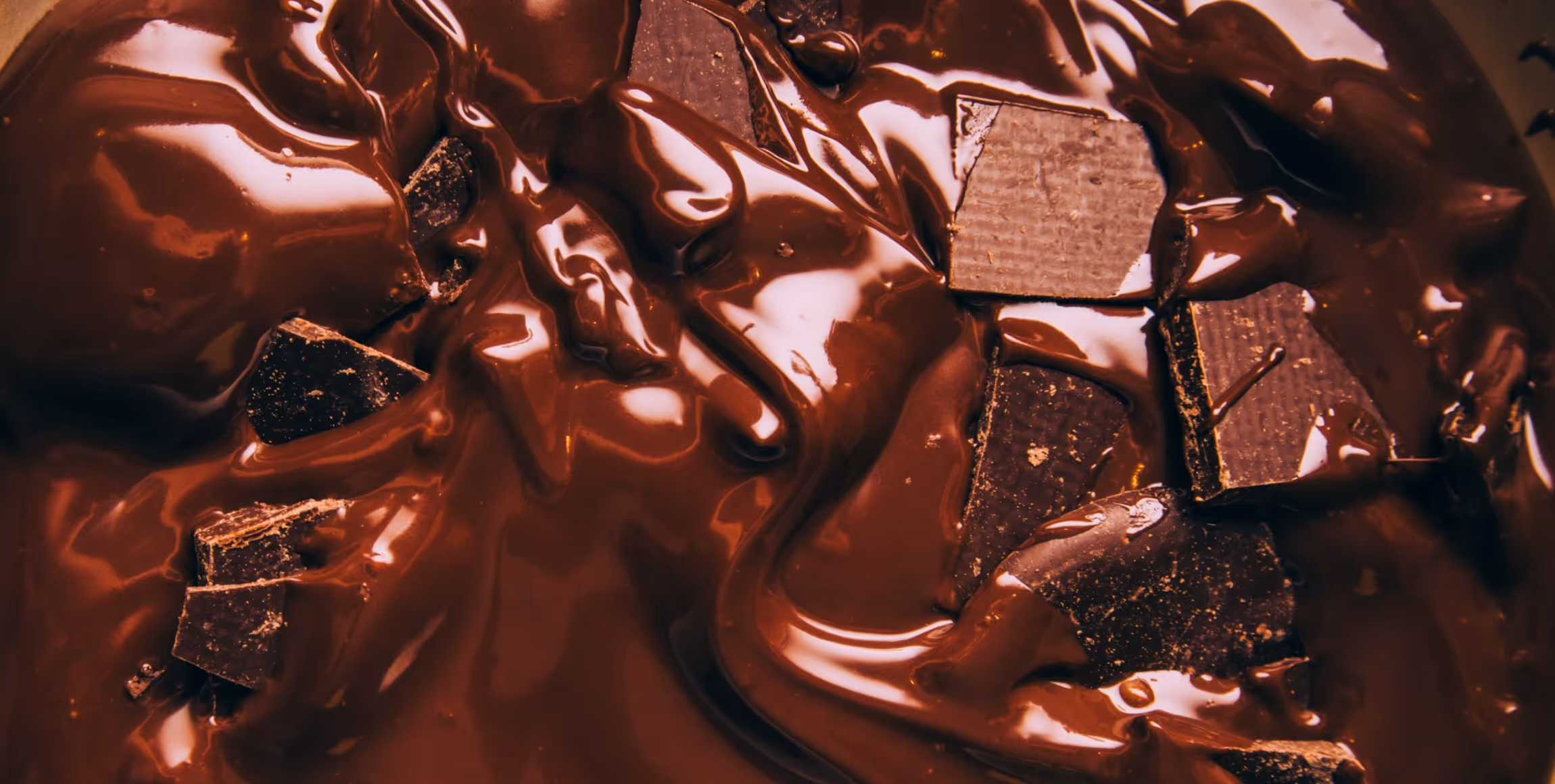 Close-up of dark chocolate chunks melting in glossy, melted chocolate.