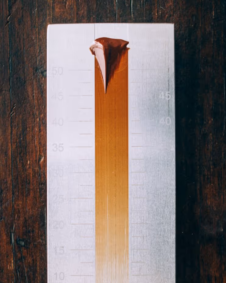 Vertical gradient of brown paint swatch on a white card placed on a dark wooden surface.