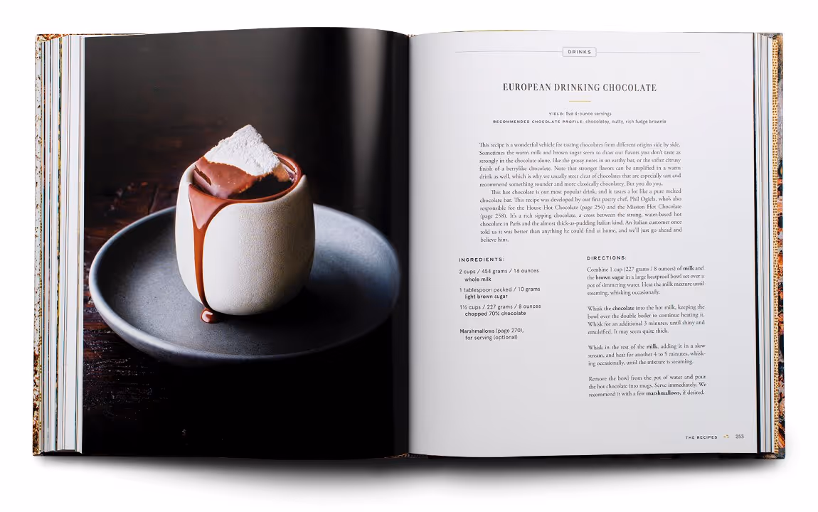 Open cookbook displaying a European drinking chocolate recipe on the right page and a photo of a ceramic mug filled with melted chocolate and topped with a marshmallow on the left page.