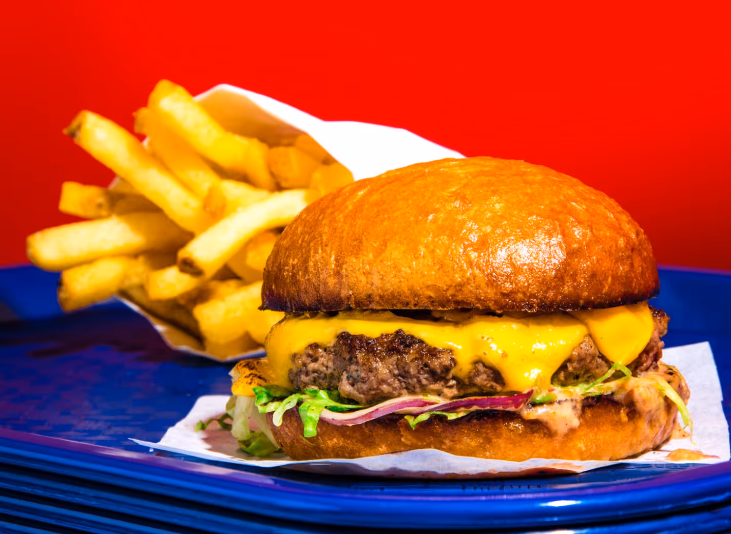 Cheeseburger with melted cheddar, lettuce, and onions on a brioche bun, served with a side of golden French fries on a blue plate.