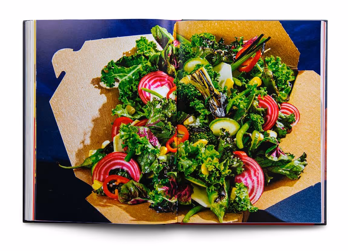 Open book showing a colorful fresh vegetable salad with kale, striped beets, red peppers, corn, and grilled onions on brown paper.