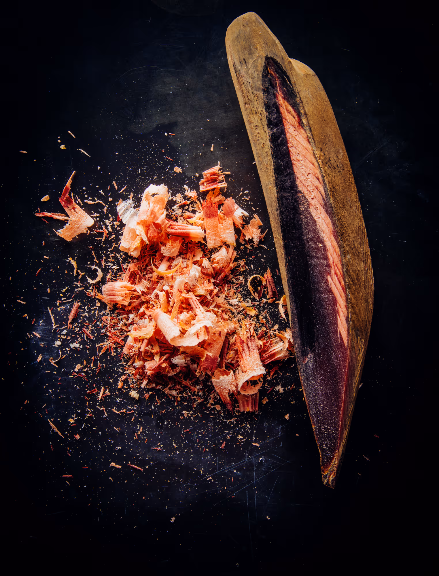 Half of a cocoa pod with reddish-brown cocoa bean husks scattered on a dark surface.