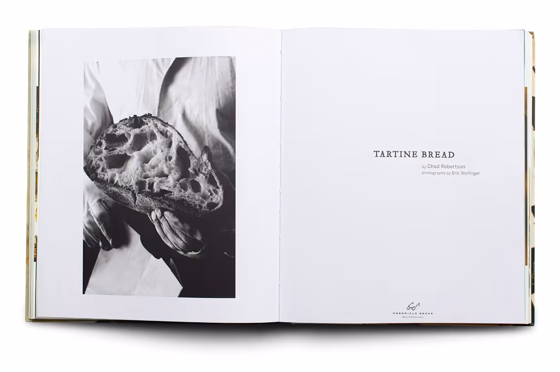 Open book showing a black-and-white photo of hands holding a loaf of bread on the left page, and the title 'TARTINE BREAD' with author and photographer credits on the right page.