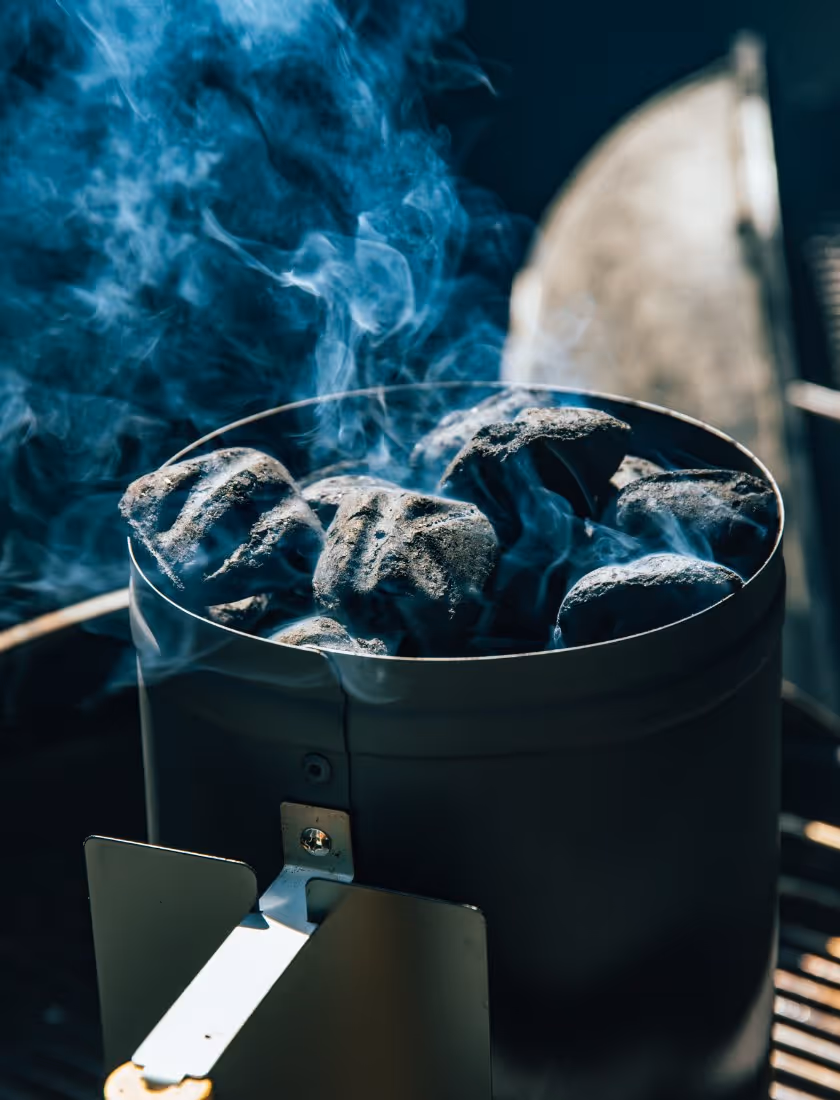 Charcoal briquettes glowing with smoke in a chimney starter on a grill.