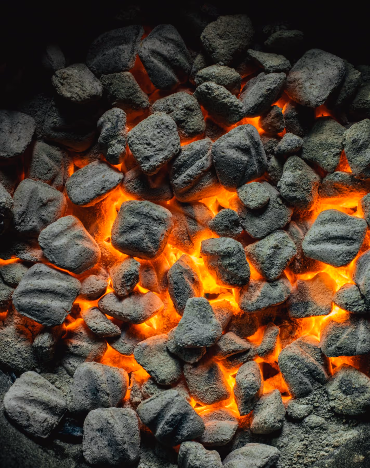 Hot glowing charcoal briquettes with bright orange flames visible between them.