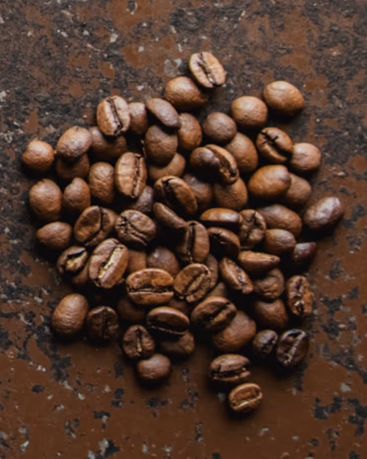 Close-up of roasted coffee beans on a textured brown surface.