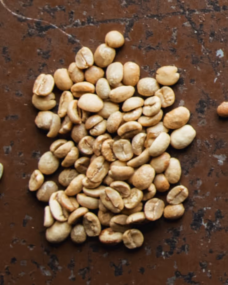 Close-up of a small pile of raw, unroasted coffee beans on a textured brown surface.