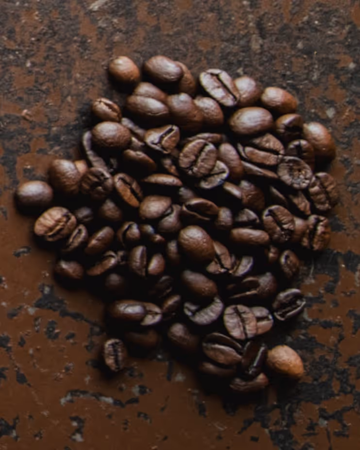 Close-up of roasted coffee beans scattered on a textured brown surface.