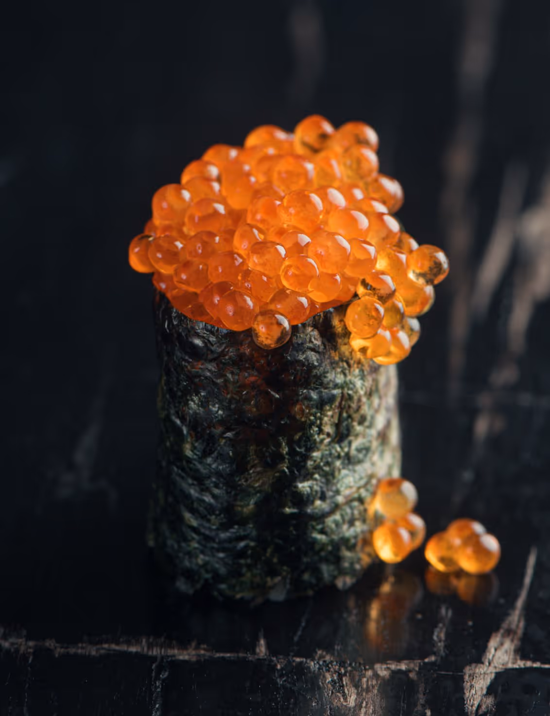Close-up of a sushi piece topped with orange fish roe on a dark surface.