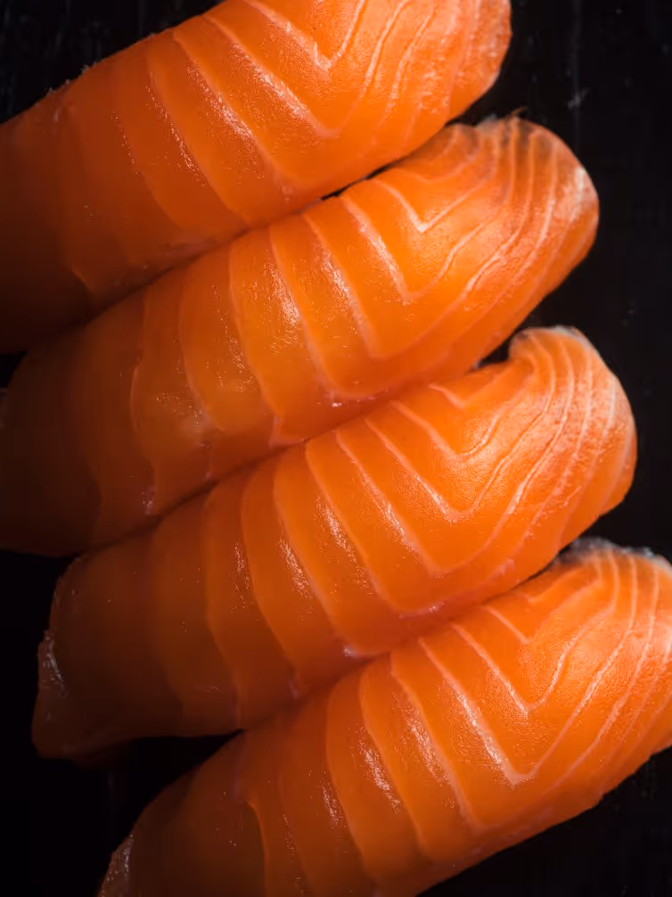 Close-up of four pieces of fresh, orange salmon sashimi with fine white lines on a black surface.
