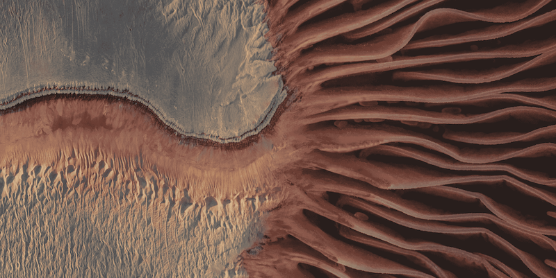 Aerial view of sand dunes transitioning from smooth beige to dark brown rippled patterns.