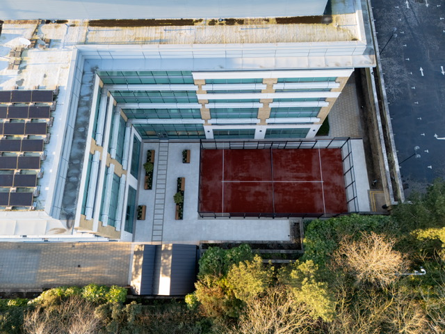 Dark red outdoor padel court shown from above, within a block of apartments