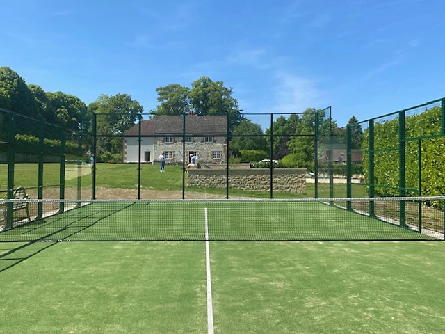 Padel court installed in a private residence, sun is shining over a green turf court with house to the rear.