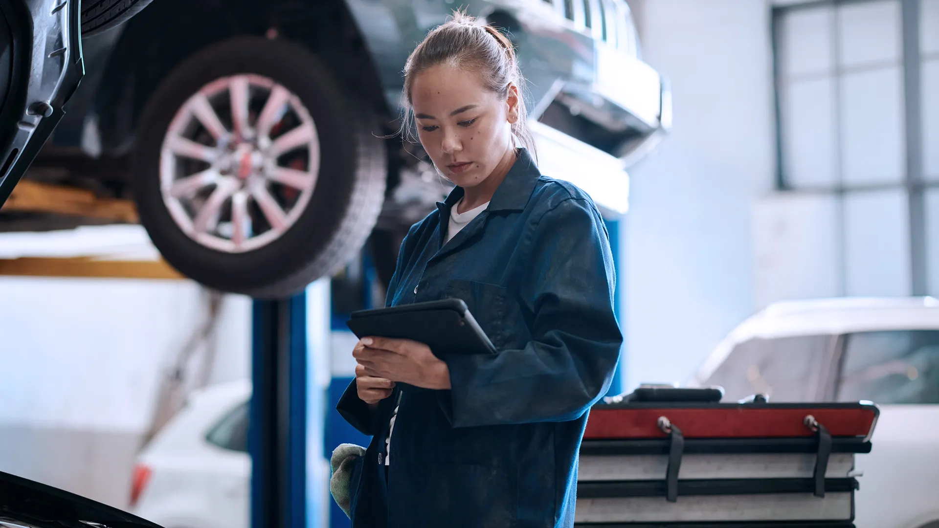Mechanic using a tablet in a modern auto repair workshop connected to an electronic spare parts catalog infrastructure