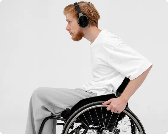 Man with red hair and beard wearing a white shirt and headphones, sitting in a wheelchair and pushing the wheel.