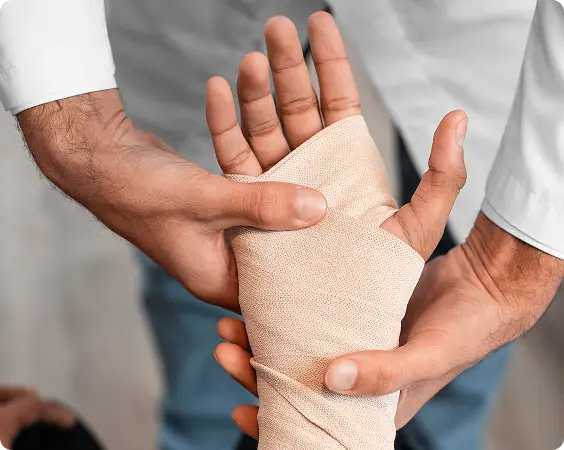 Person's hand wrapped in a beige bandage being held and supported by another person's hands.