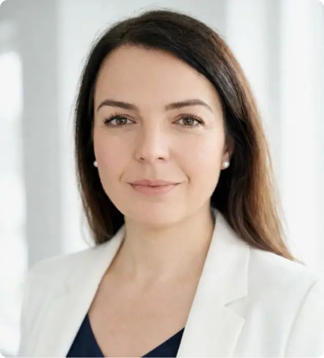 Professional woman with long dark hair wearing pearl earrings, a white blazer, and a dark top, smiling softly against a bright background.