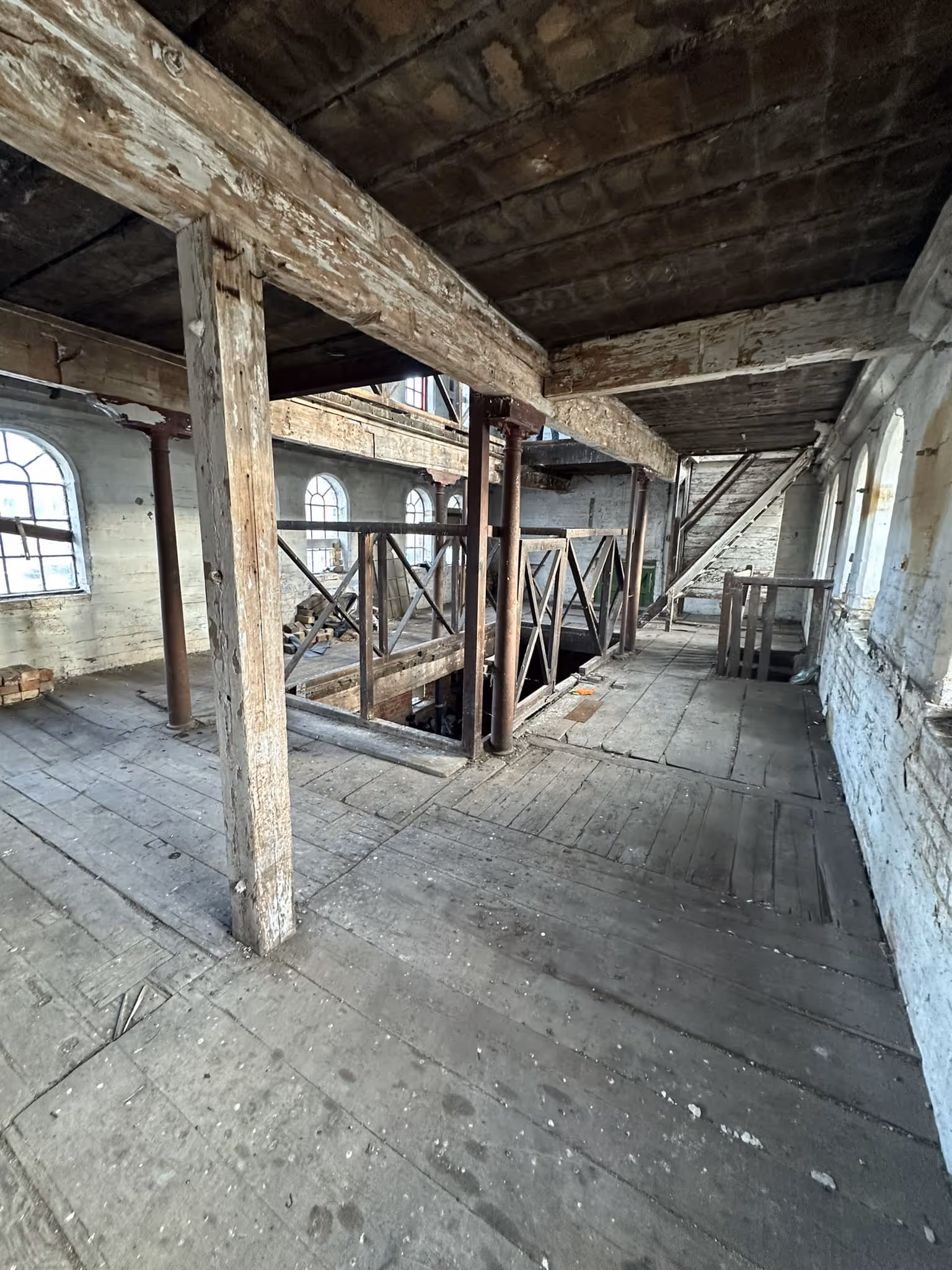 Interior of an old, abandoned wooden building with peeling paint, exposed beams, and multiple arched windows letting in natural light.