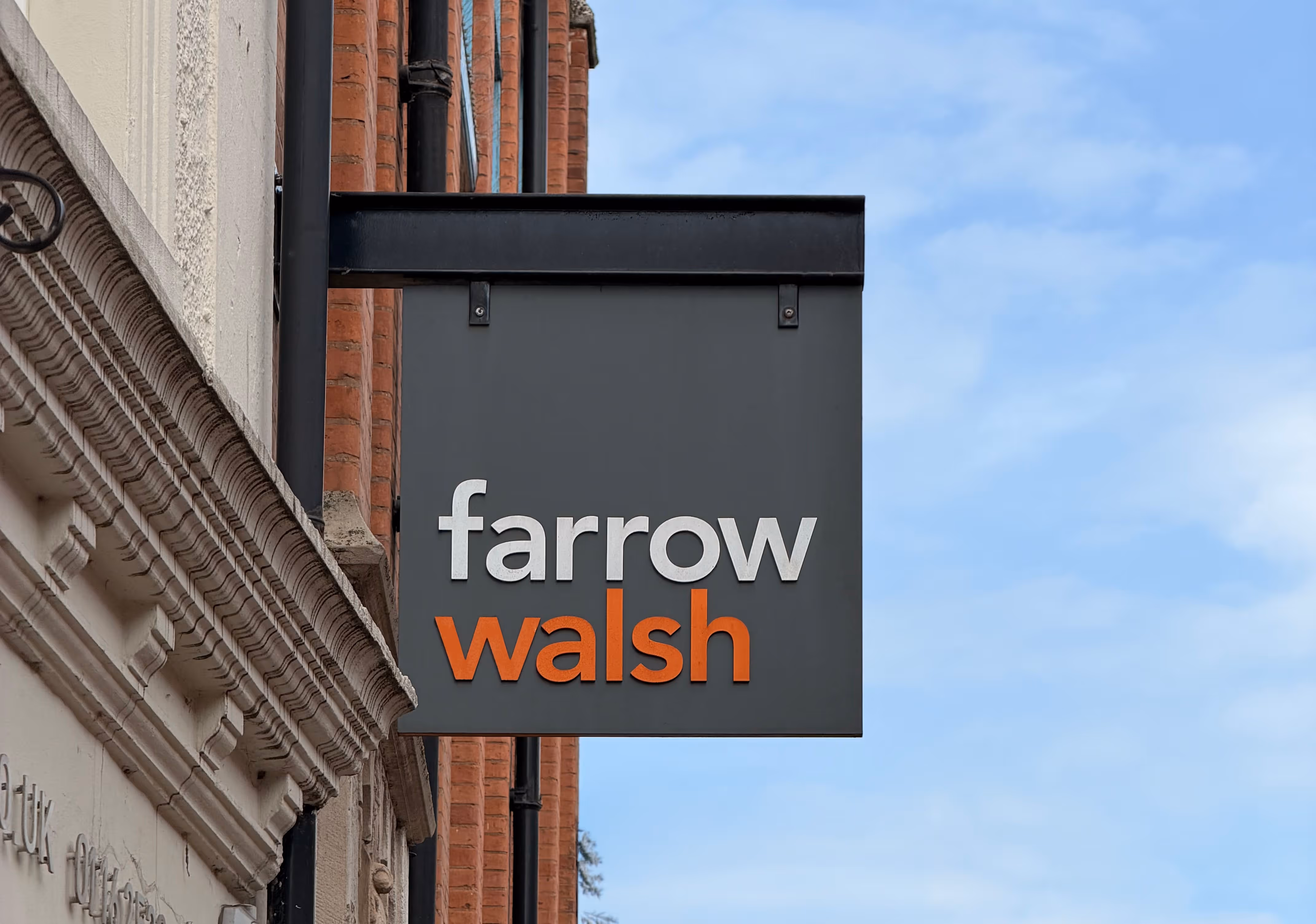 Street sign with the text 'farrow walsh' mounted on a building with a blue sky background.