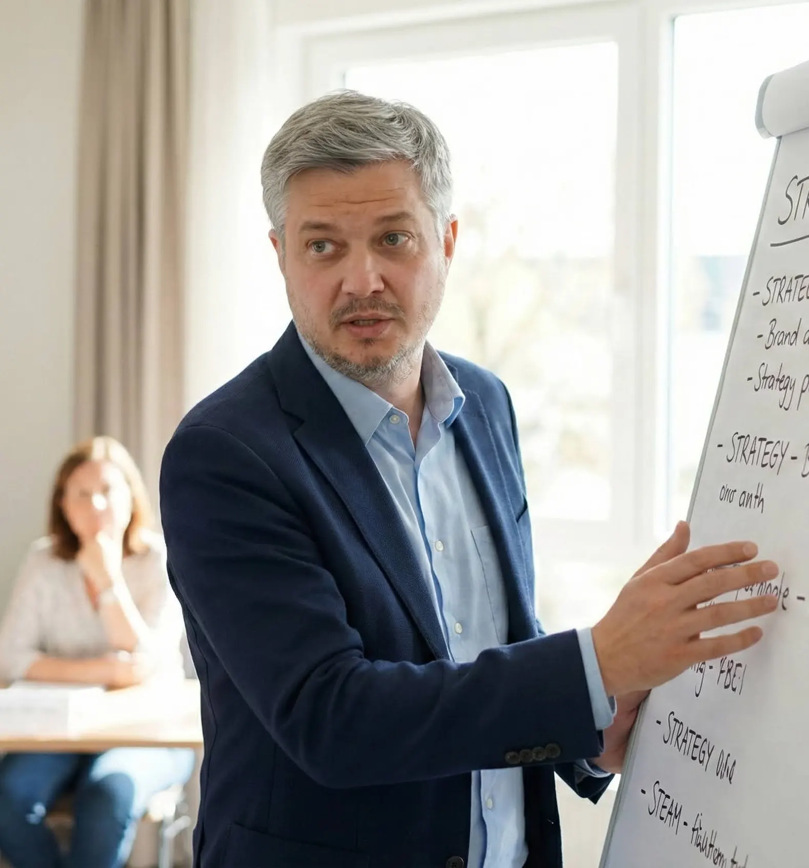 Mann erklärt etwas an einem Whiteboard mit Listenpunkten, im Hintergrund sitzt eine Frau und hört zu.