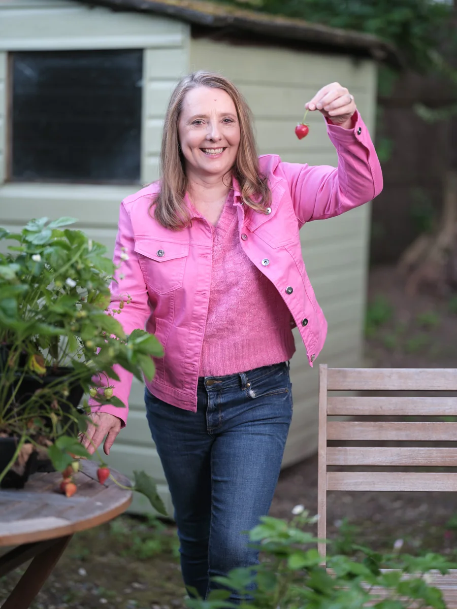 Ailsa Frank holding a strawberry in a garden