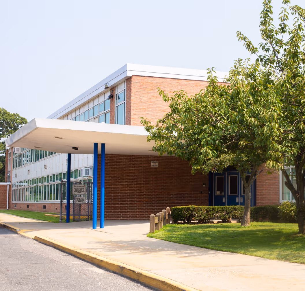 Entrance of a modern brick school building with blue doors, large windows, and a covered walkway supported by blue pillars.