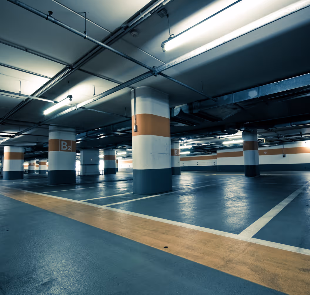 Empty underground parking garage with marked parking spaces and support columns painted white, orange, and gray.