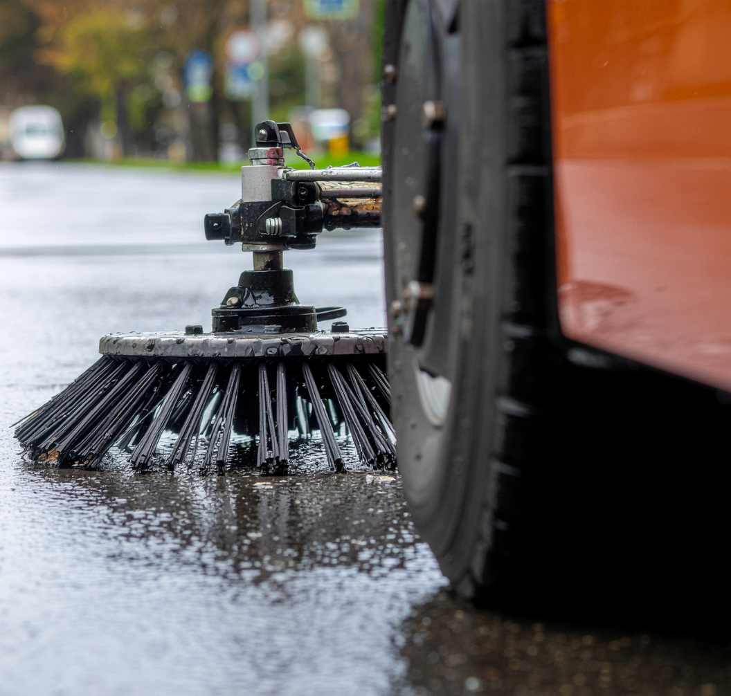 Close-up of a street sweeper brush and tire cleaning a wet urban road surface.