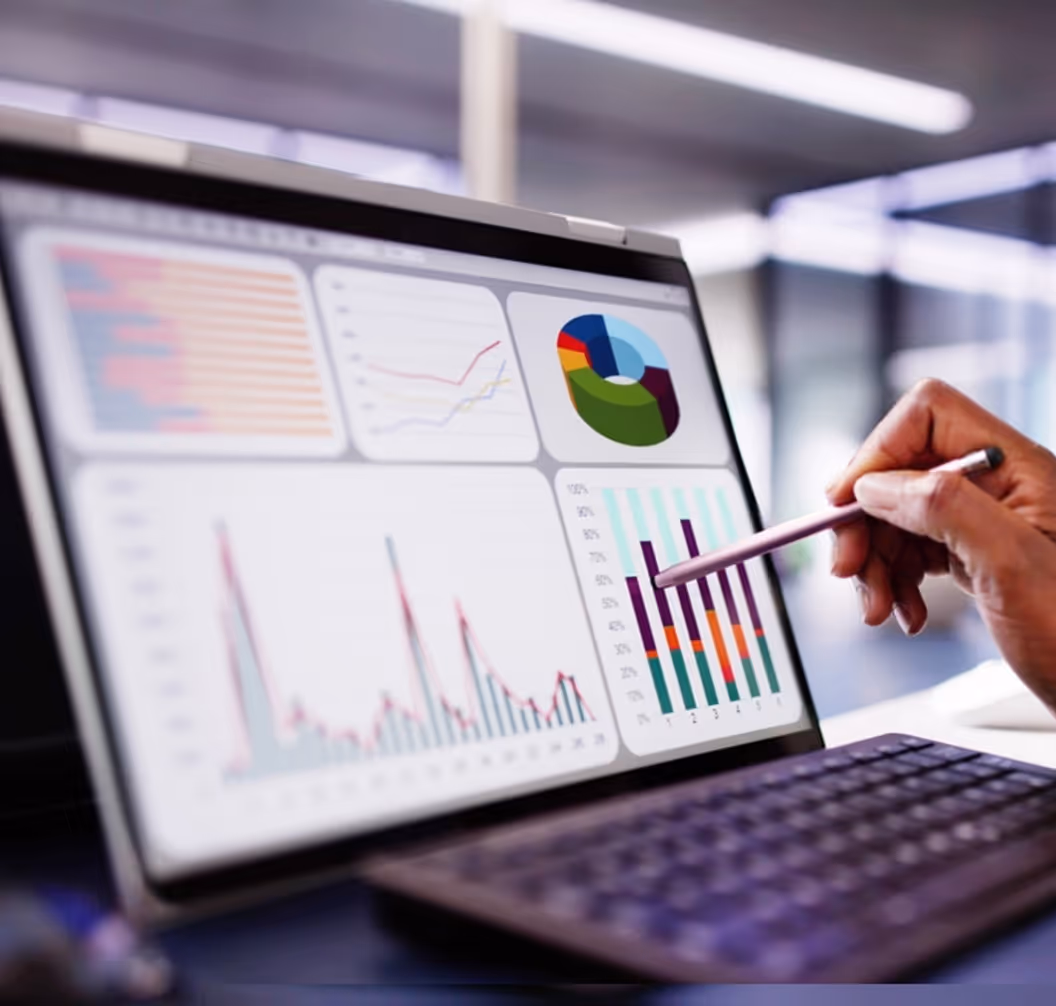 Person holding a stylus and pointing at colorful graphs and charts displayed on a computer screen.