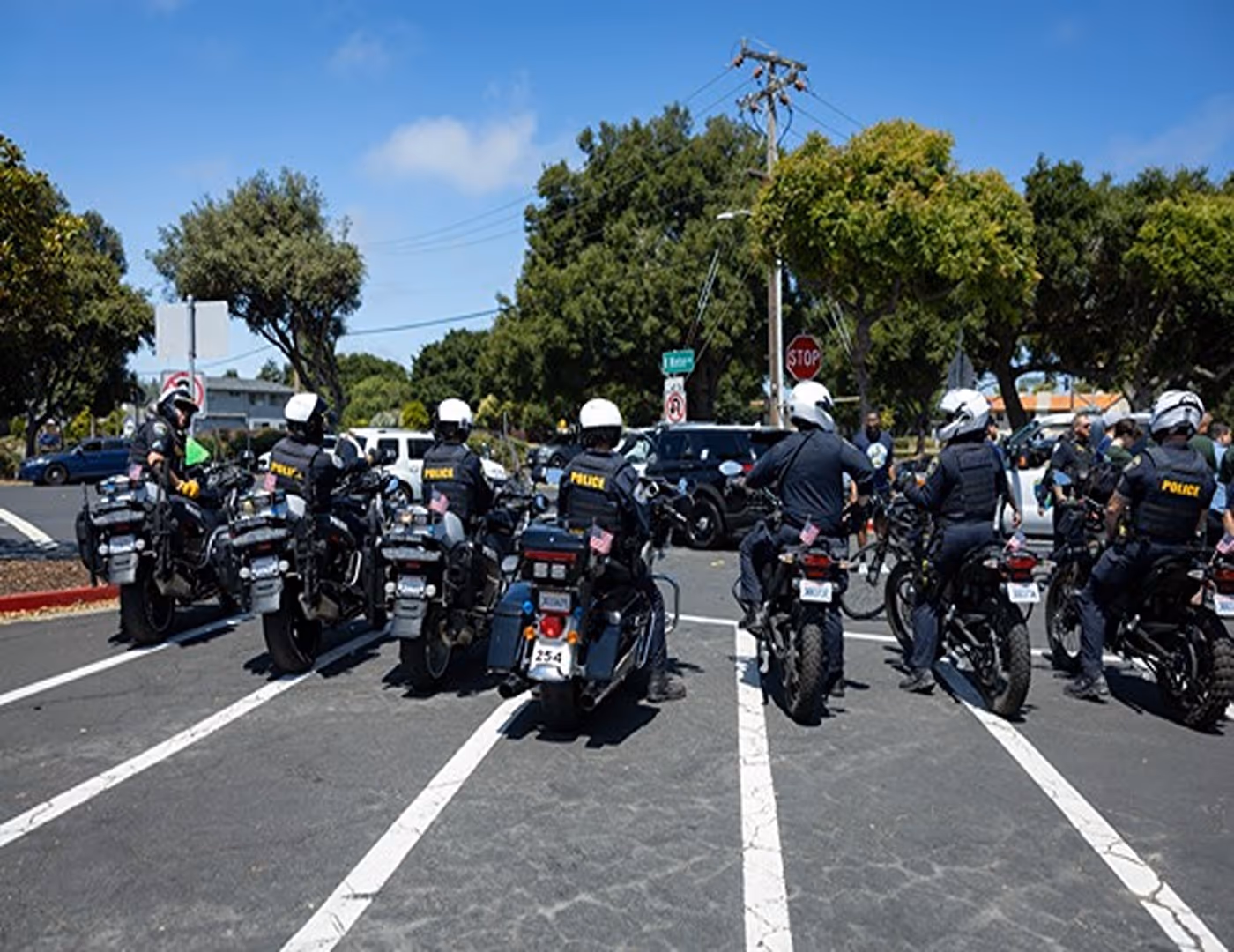 Group of police officers on motorcycles stopped at an intersection on a sunny day.