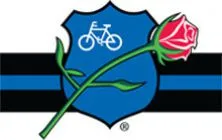 Blue police shield with a white bicycle icon and a red rose crossing the shield and thin blue line flag in the background.